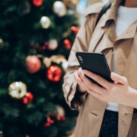 przycięte ujęcie i środkowa część kobiety korzystającej ze smartfona przed kolorową choinką w świątecznym okresie świątecznym
