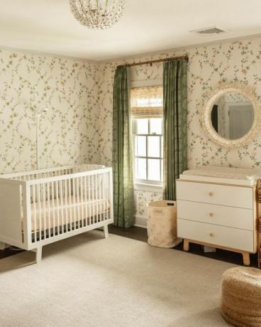 pokój dziecinny, tapeta w kwiaty, zielone zasłony, białe łóżeczko, biało-drewniana komoda, dywan w kolorze nude