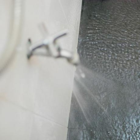 wyciekająca woda z kranu rozpryskująca się na podłogę w łazience z powodu pękania pod wysokim ciśnieniem