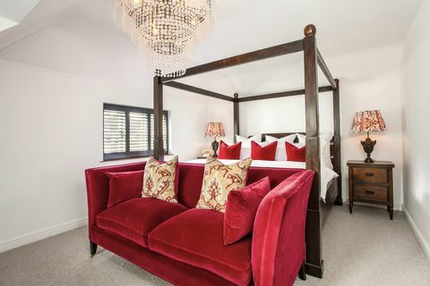 biała sypialnia z łóżkiem z baldachimem i czerwoną sofą