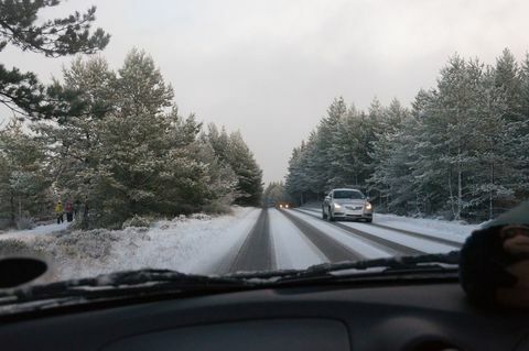 Samochód jedzie po drodze pokrytej śniegiem wśród drzew