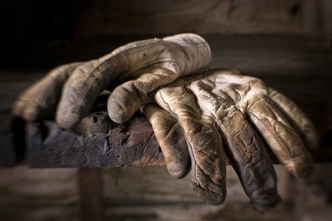 Dobrze zużyte, brudne i tłuste rękawice robocze na starej ławce roboczej.