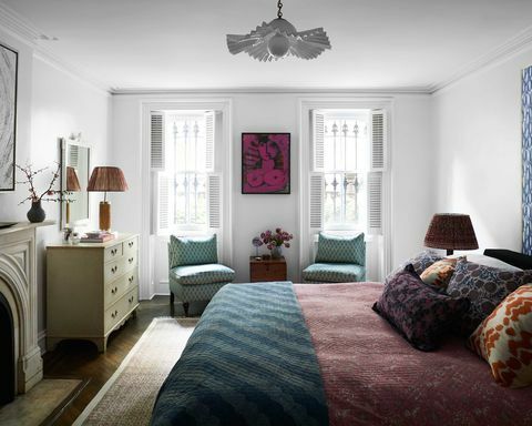 sypialnia, niebieskie krzesła do siedzenia, czerwona pościel, zielony dywanik, poduszki dekoracyjne, kominek, biała lampa sufitowa