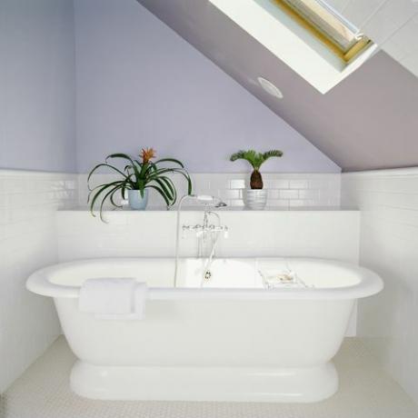 Wanna pod świetlikiem w łazience na poddaszu z liliowo-fioletowymi ścianami