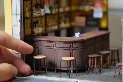 zbliżenie miniaturowej repliki baru ze stołkami barowymi i ludzką ręką do skali