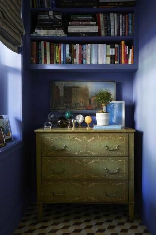 ściany pomalowane na niebiesko, zielona komoda, marmurowe kule, ozdobne książki, biała roślina doniczkowa