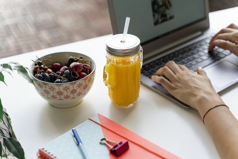 Zakończenie kobieta używa laptop przy biurkiem z sokiem pomarańczowym i owoc