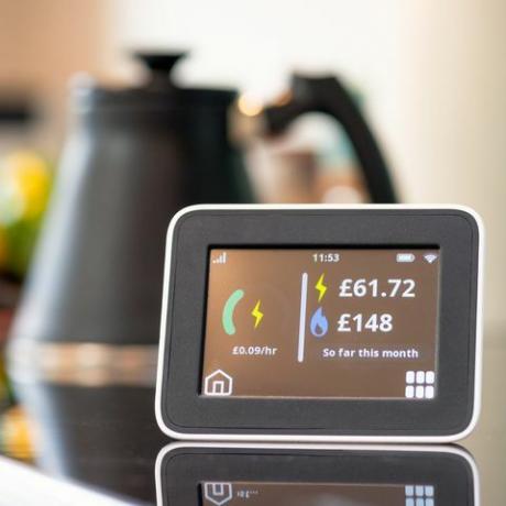 zbliżenie ekranu inteligentnego licznika w kuchni, pokazujące dotychczasowy miesięczny koszt energii elektrycznej i gazu