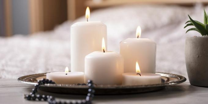 kompozycja białych płonących świec na stoliku nocnym w jasnym, przytulnym wnętrzu sypialni, selektywna ostrość